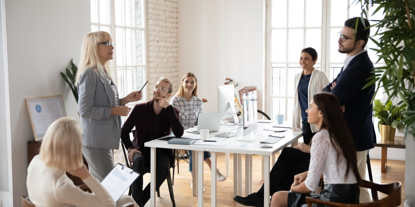 Smiling young mixed race employees discussing business ideas with middle aged supervisor in office. Happy multiracial colleagues talking about marketing research results with senior mentor coach.